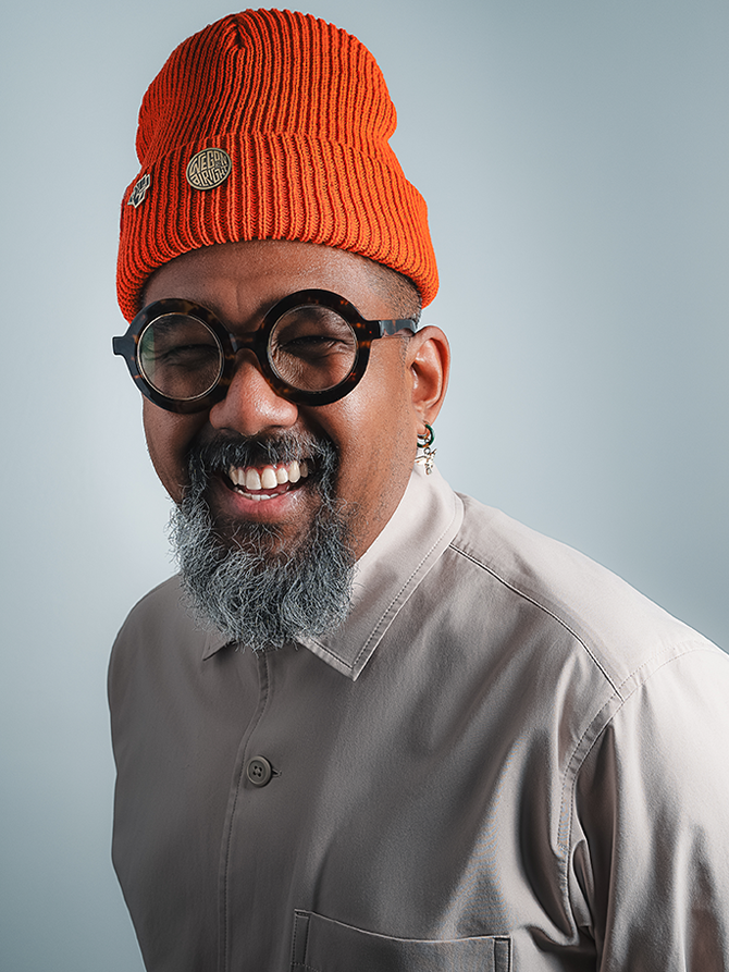 Marc Piper's Head shot. Smiling black male, wearing black baseball cap, black t-shirt and round glasses.